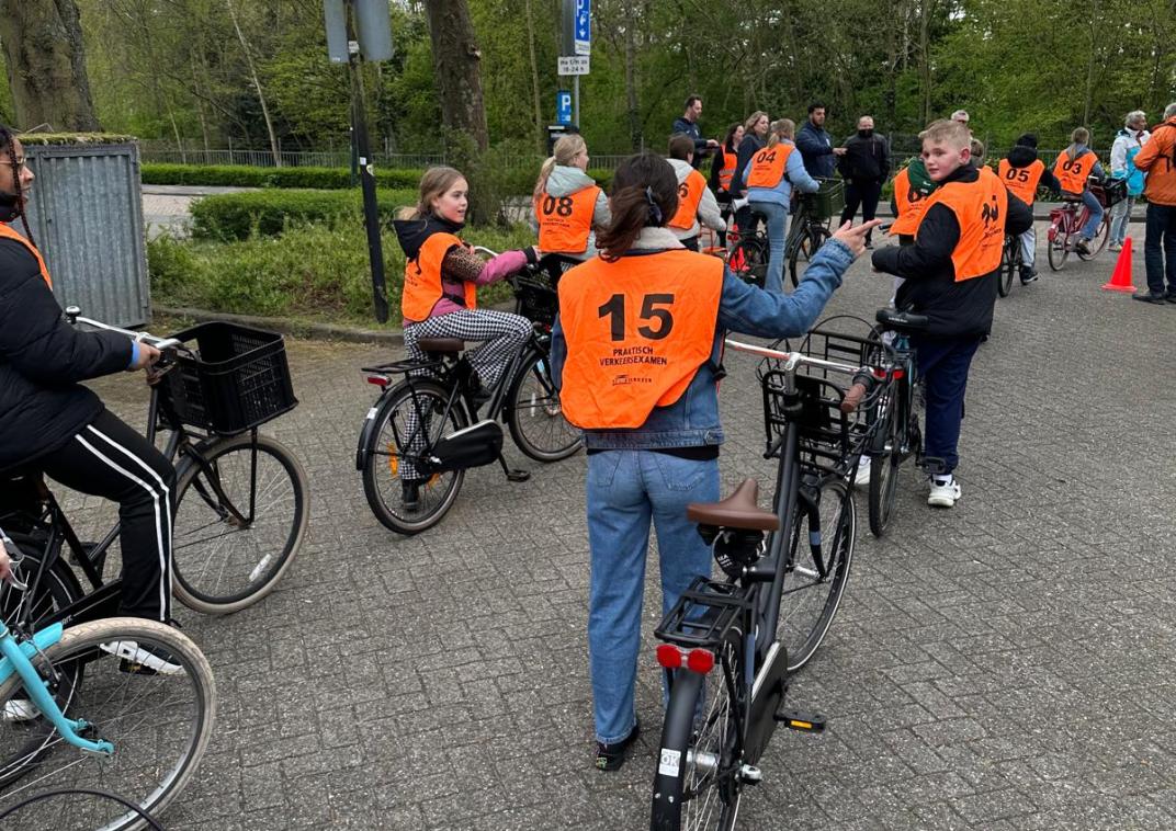 Een groep kinderen met fiets aan de hand. Ze dragen oranje hesjes.