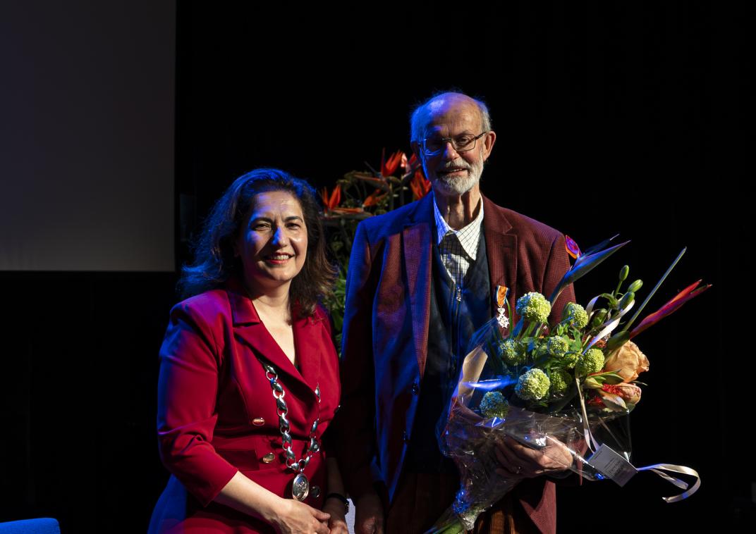 Meneer staat naast de burgemeester met een lintje en bos bloemen in handen