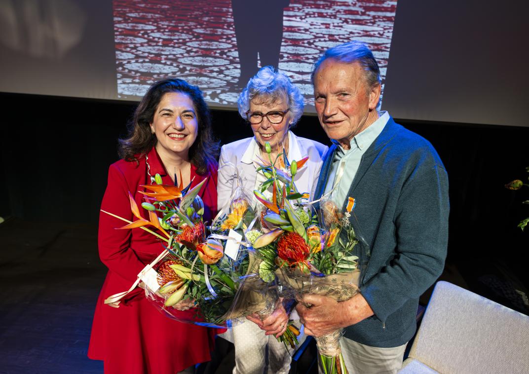 vrolijk echtpaar met lintje opgespeld en bos bloemen in de handen