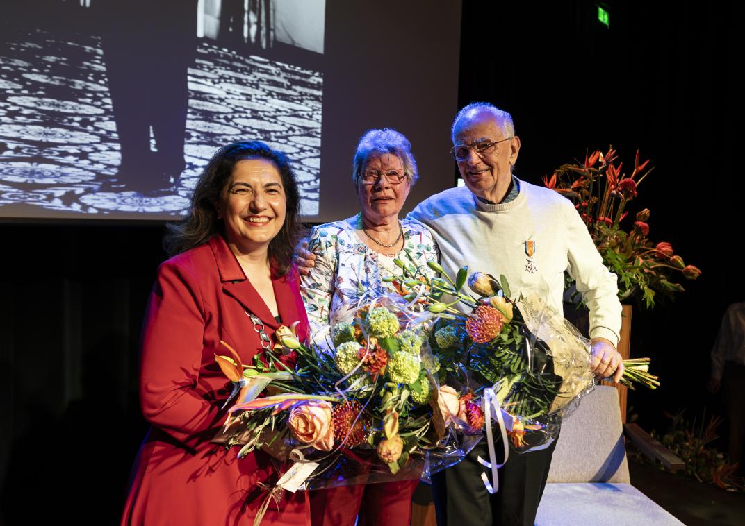 Echtpaar geposeerd met bloemen en lintje kijken vrolijk terwijl ze met de burgemeester op de foto gaan