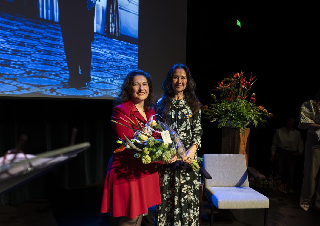 mevrouw met grote bos bloemen in handen en een lintje opgespeld