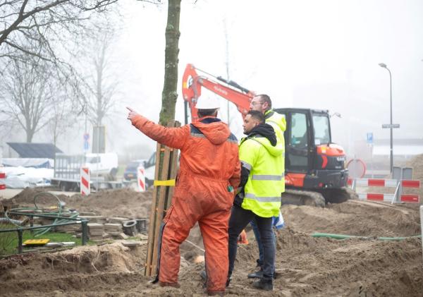 Twee mannen in oranje werkkleding staan op een bouwplaats.