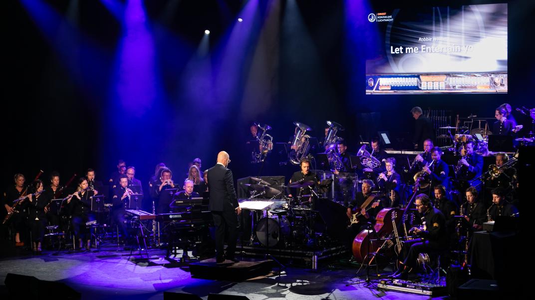 Een orkest speelt met muziekinstrumenten een lied onder begeleiding van een dirigent 