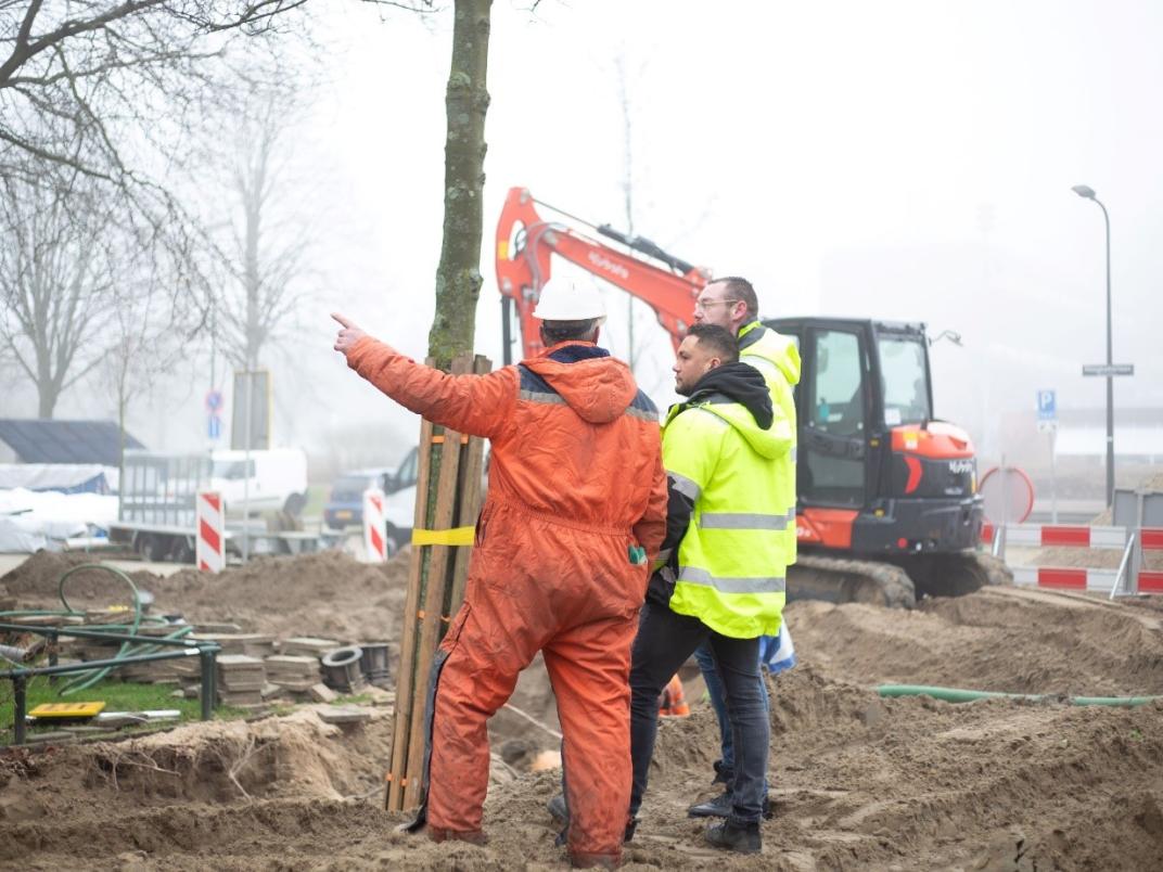 Twee mannen in oranje werkkleding staan op een bouwplaats.