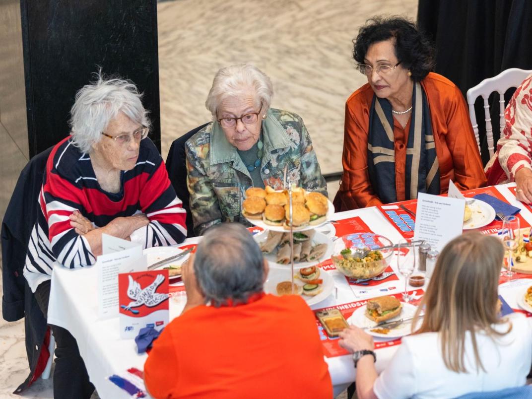 Vier oudere dames die met elkaar in gesprek zijn aan tafel.