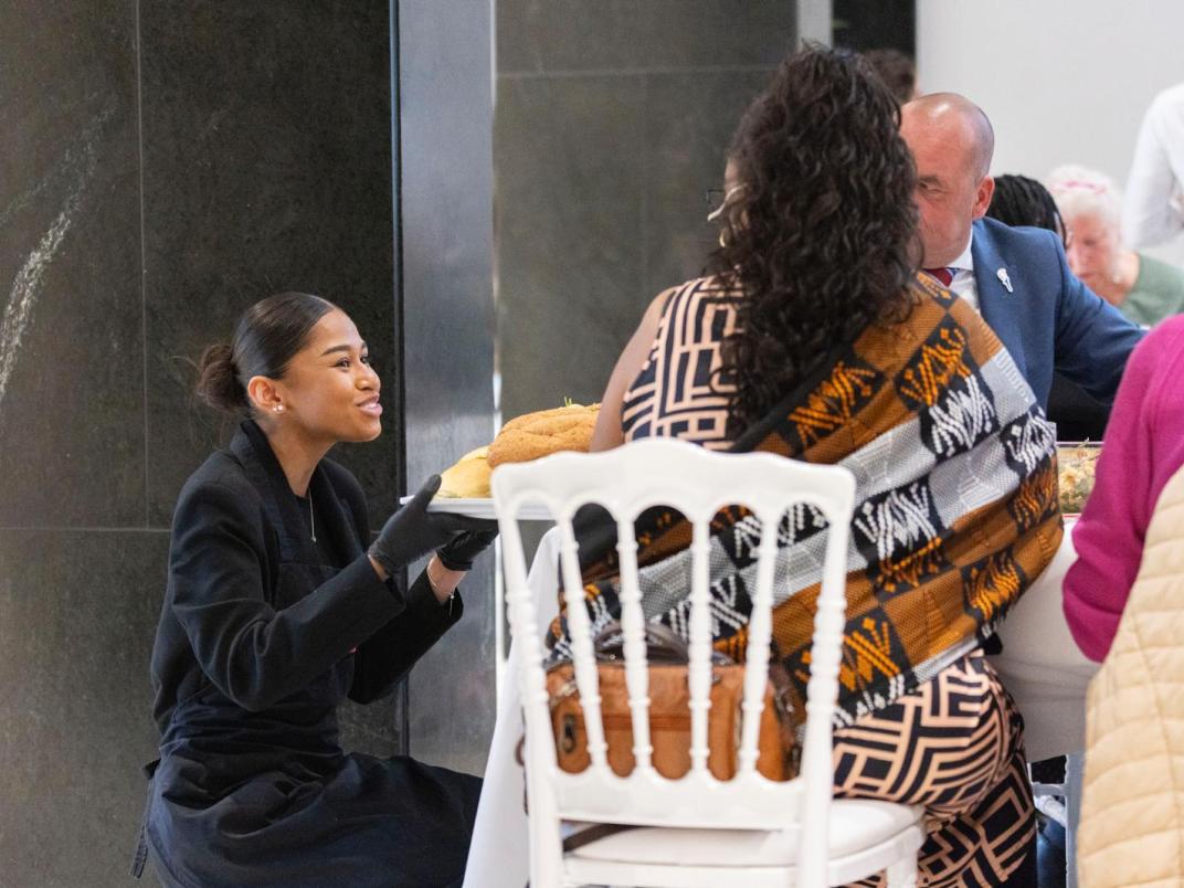 Leerling zit op haar hurken aan een tafel met een vrouw en man te praten. Ze heeft een glimlach op haar gezicht.