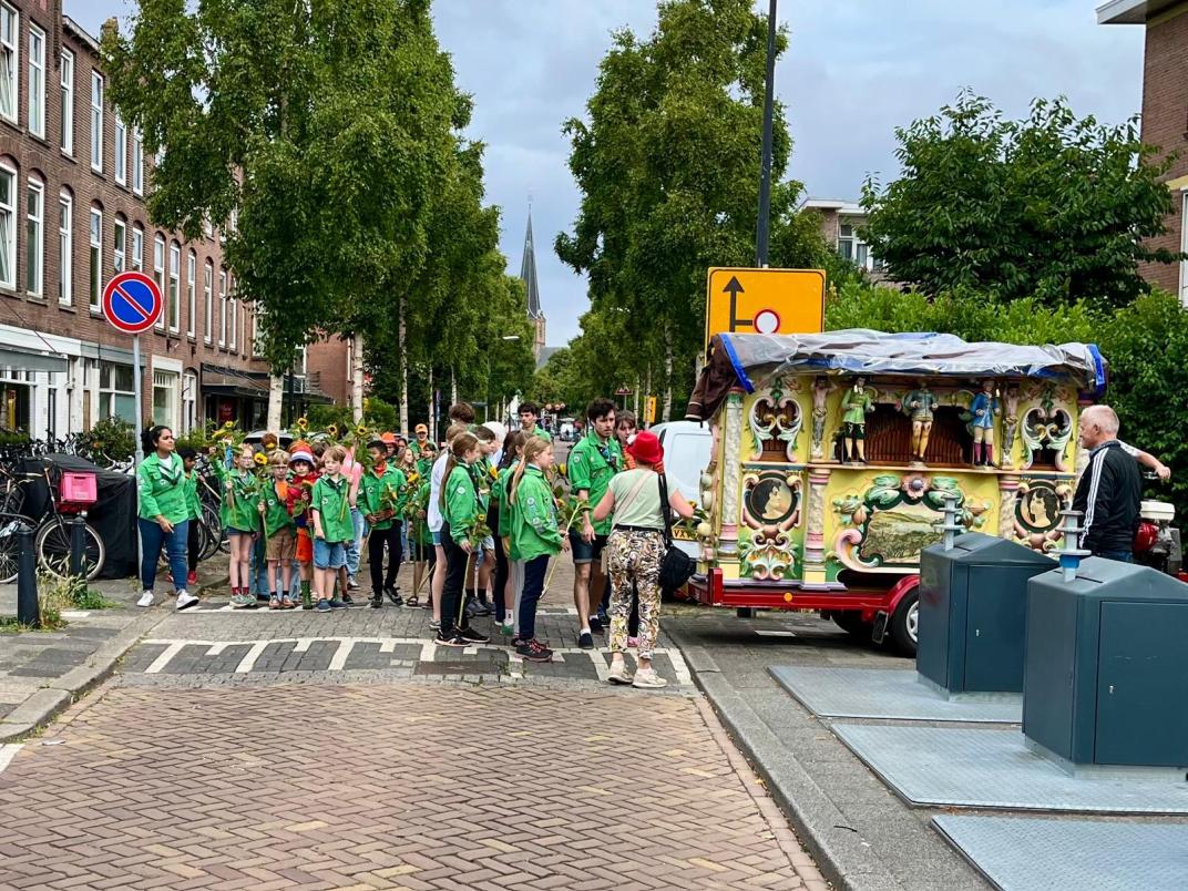 Kinderen staan bij draaiorgel op een straat naast huizen
