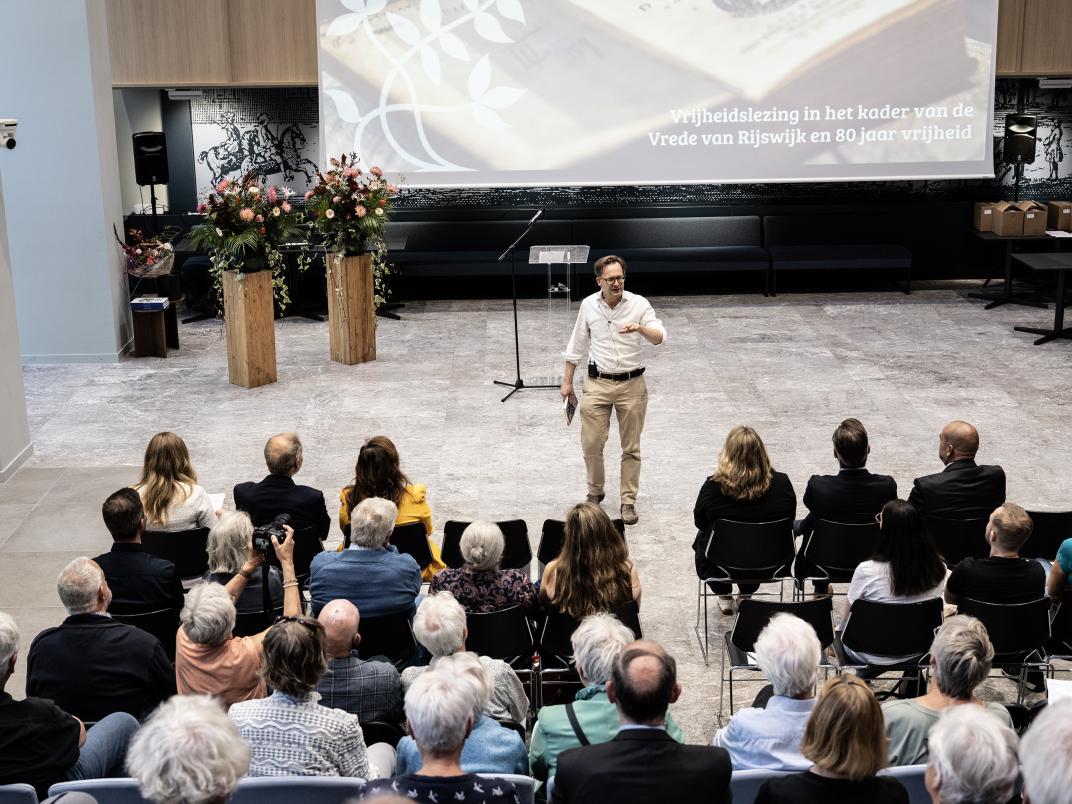 publiek in een zaal die luistert naar een man die staat te spreken