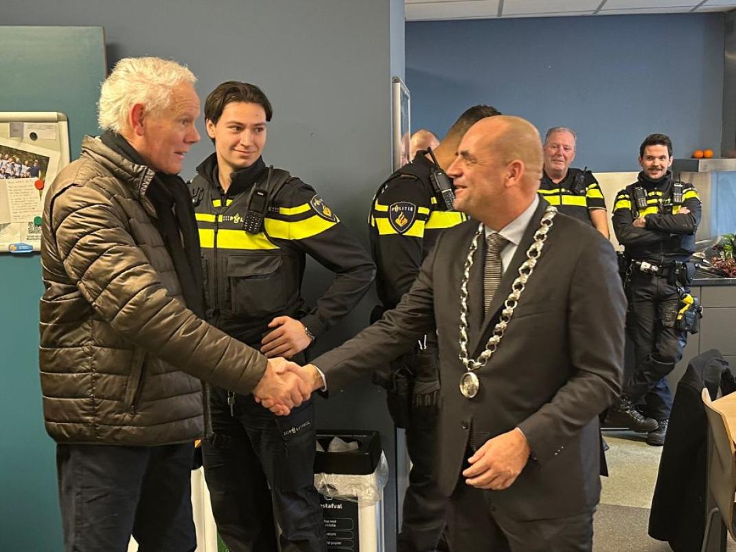 Twee mannen schudden elkaar de hand. Rechts staat de locoburgemeester en links de ontvanger van het Rijswijks Compliment. Op de achtergrond staan verschillende politieagenten.