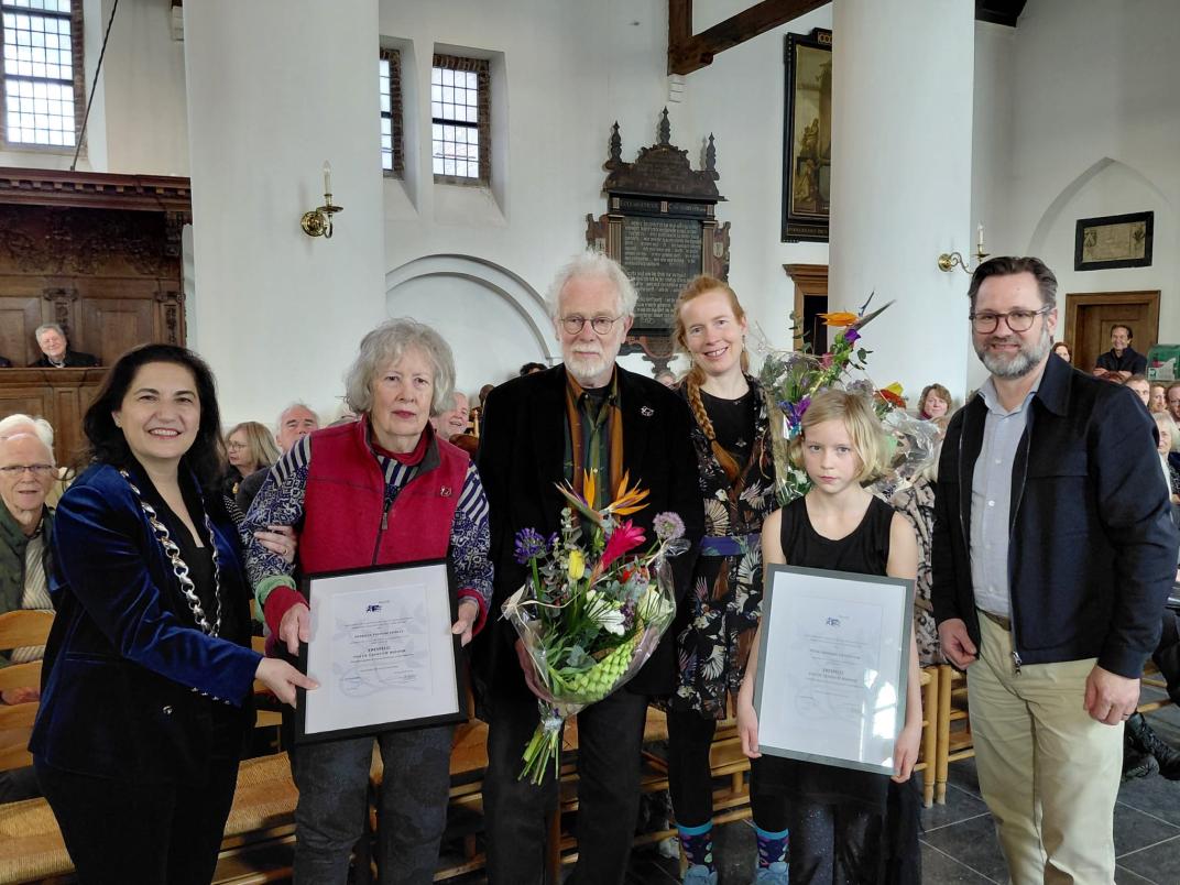 Een groep oudere mensen waarvan twee personen een oorkonde vasthouden ter ere van de uitreiking van de Rijswijkse Erespeld