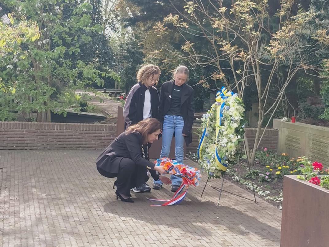Een bloemenkrans wordt door twee kinderen en de burgemeester bij een monument gelegd.