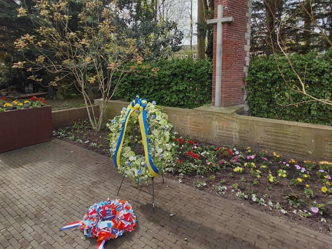 Een bloemenkrans staan en liggen voor een oorlogsmonument. 
