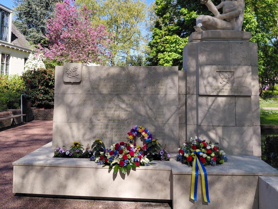 Een oorlogsmonument daar verschillende bloemenkransen omheen liggen.