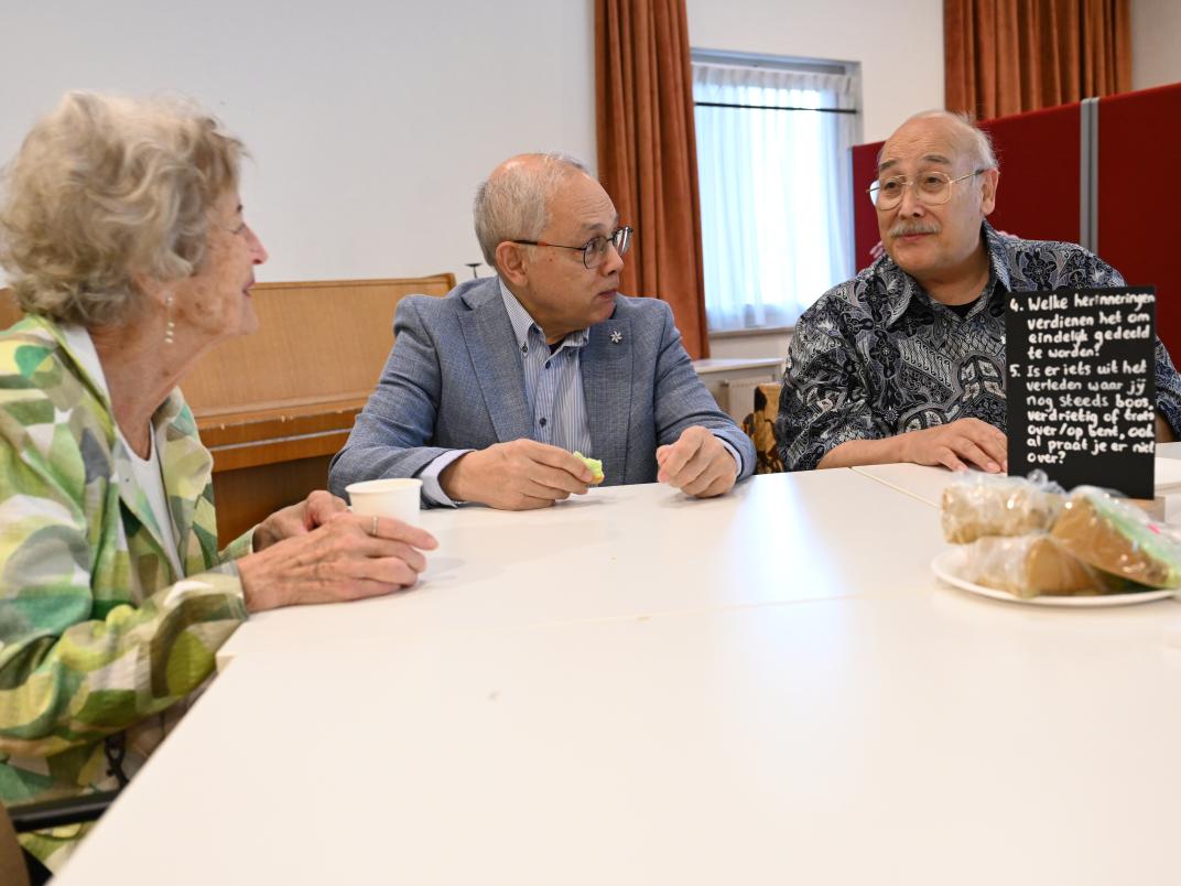 Twee senioren mannen en een seniore vrouw zijn met elkaar in gesprek.