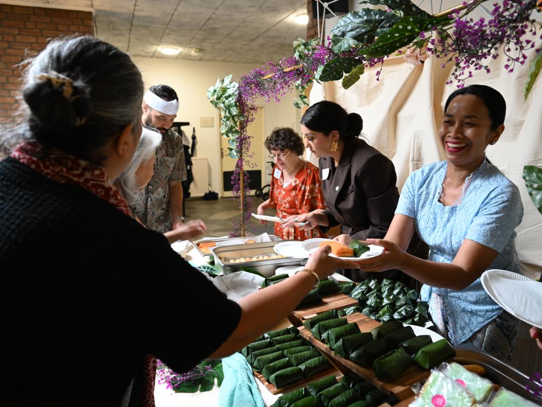 Een Indonesische vrouw geeft met een grote glimlach op haar gezicht een bord met eten aan een vrouw.