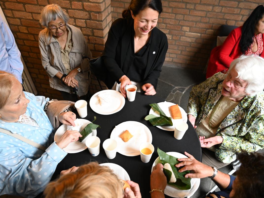 Een groep mensen is met elkaar in gesprek en hebben borden met Indonesisch eten voor zich staan.
