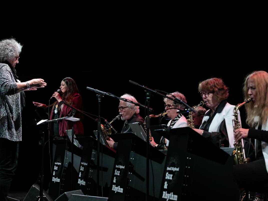 Overzichtsfoto van een orkest dat saxofoon bespeeld, een dirigent en zangeres.