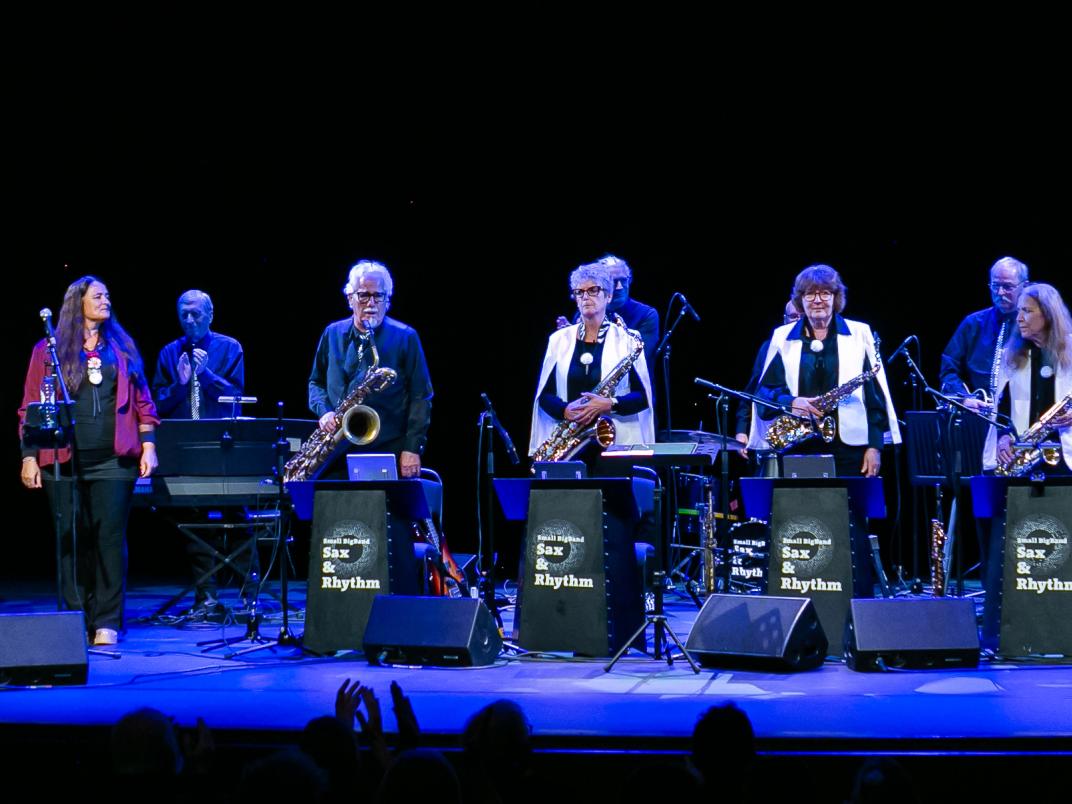 Overzichtsfoto van een orkest dat saxofoon bespeeld, een dirigent en zanger.