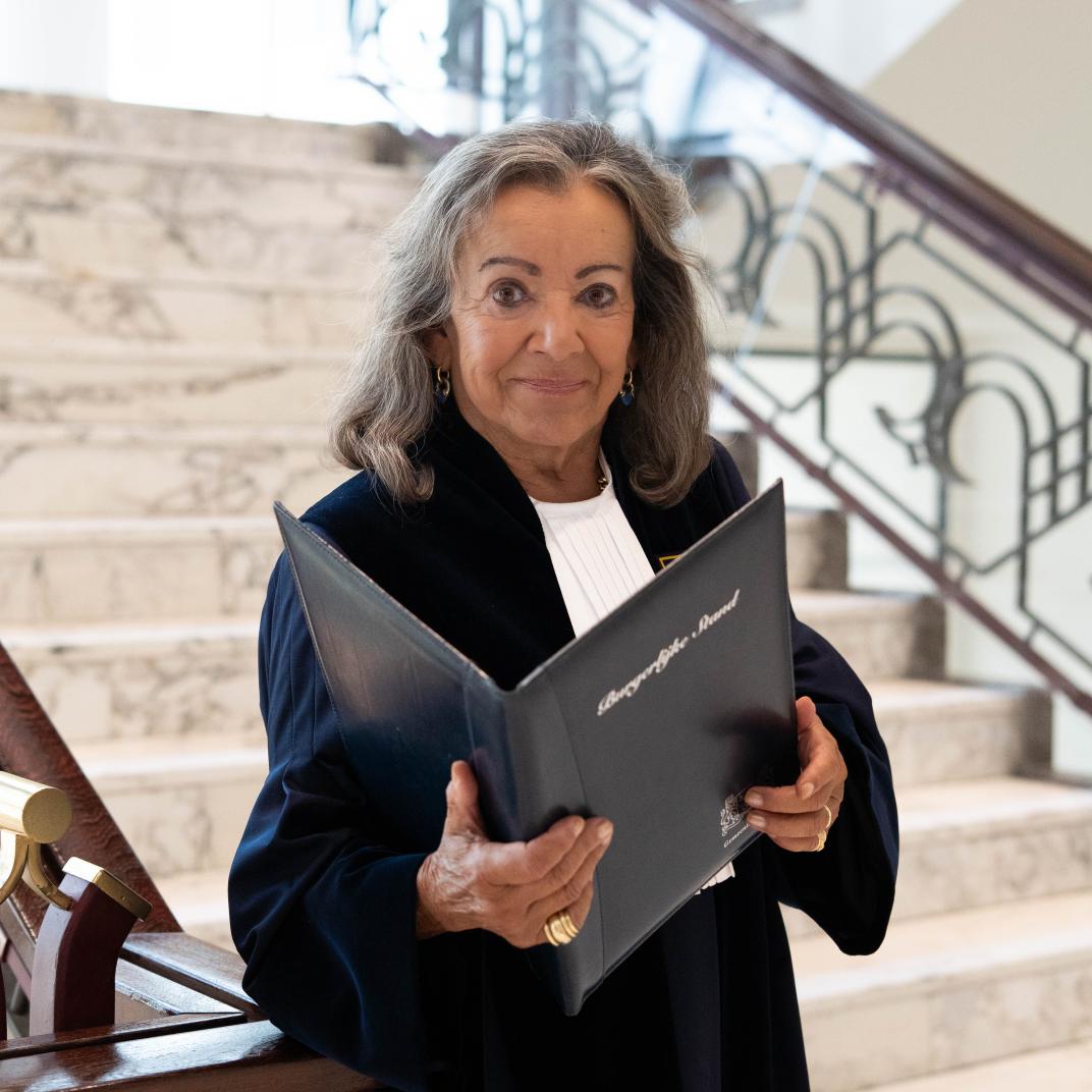 Mevrouw met officiële toga aan en een map in haar handen die staat op de trap in het Huis van de stad
